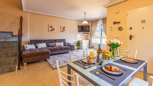 A modern living room with a sofa, a dining table set for breakfast, and a TV mounted on the wall. - 3 bedroom amazing home in Orihuela Costa (Orihuela Costa)
