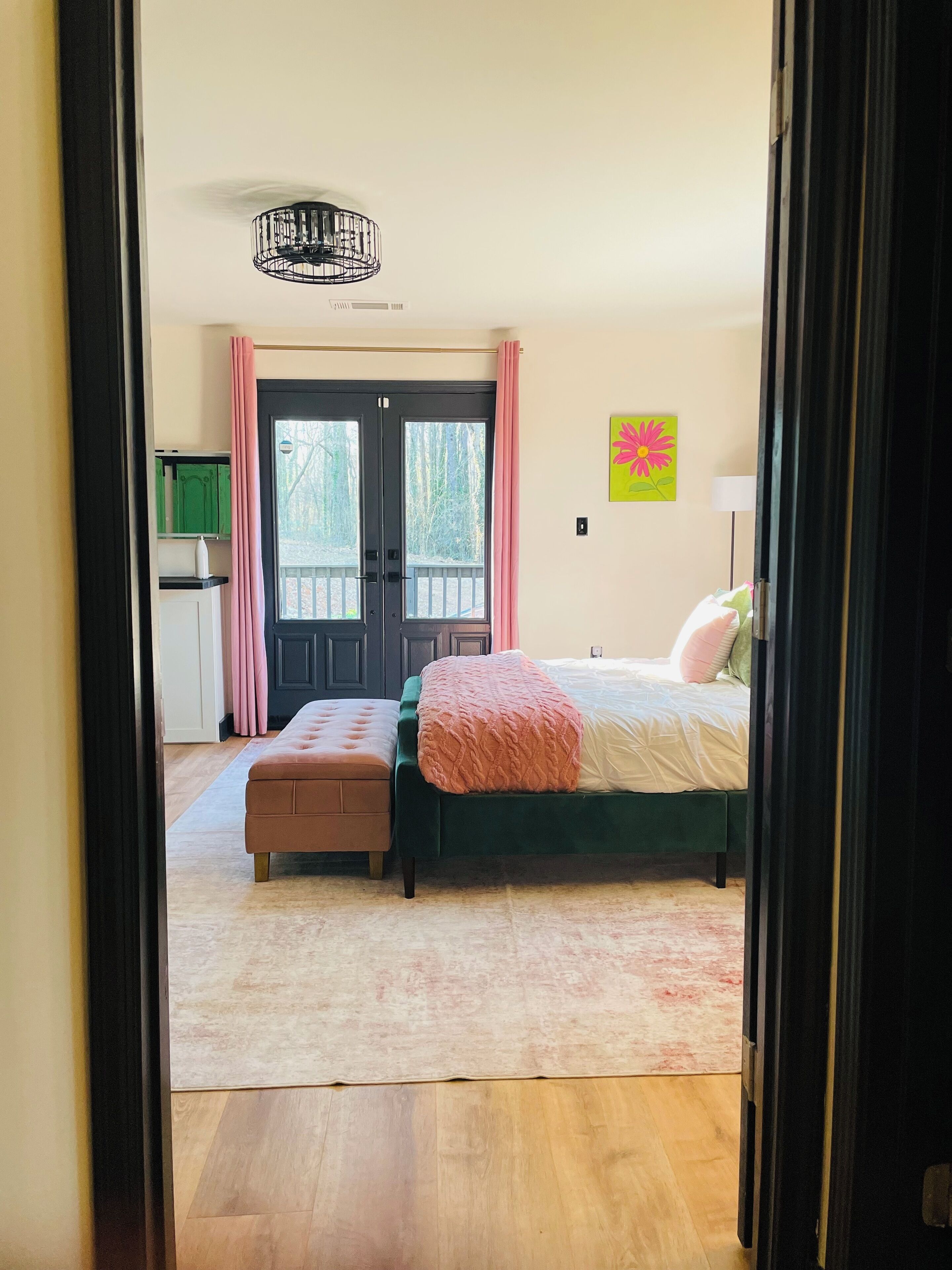 A bedroom with a bed, a bench, a door, and a view of the outside.