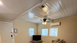 A living room with a sofa, a television, a ceiling fan, and a small table with a tissue box.