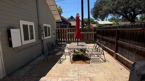 A patio area with a brick floor, a table with chairs, a red umbrella, and a wooden fence.