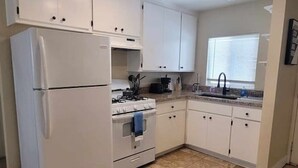 A kitchen with white cabinets, a refrigerator, an oven, and a sink.