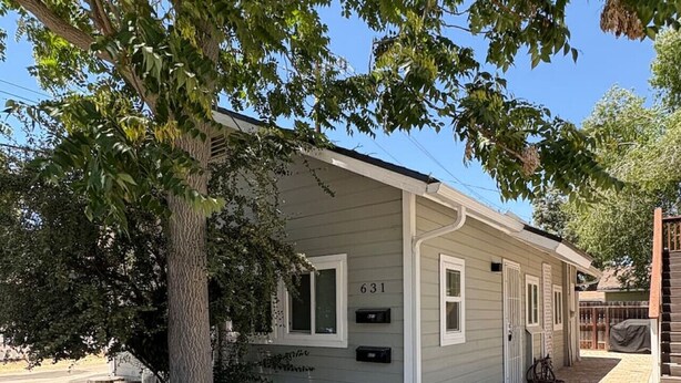 A single-story house with a number 631 on the door, surrounded by gravel and trees.
