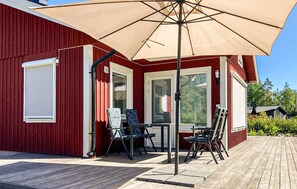 A covered outdoor seating area with a table and chairs, a large umbrella, and a wooden deck. - 2 bedroom stunning home in Mönsterås (Mönsterås)