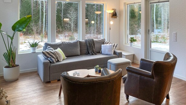 A modern living room with a grey sofa, two armchairs, and a coffee table. There are large windows with views of trees and a snowy landscape. - 2 bedroom stunning home in Mönsterås (Mönsterås)
