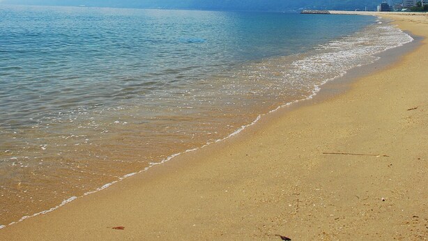 Uma praia com águas azul-claras, areal arenoso e uma montanha ao fundo.