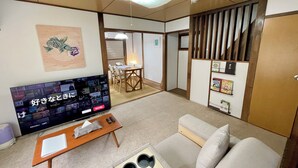 Sala de estar com televisão, sofá e área de jantar ao fundo.