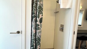 A bathroom with a shower curtain featuring a leaf pattern, a white towel hanging on the wall, and a visible door handle. - Midway Motel Rotorua (Rotorua)