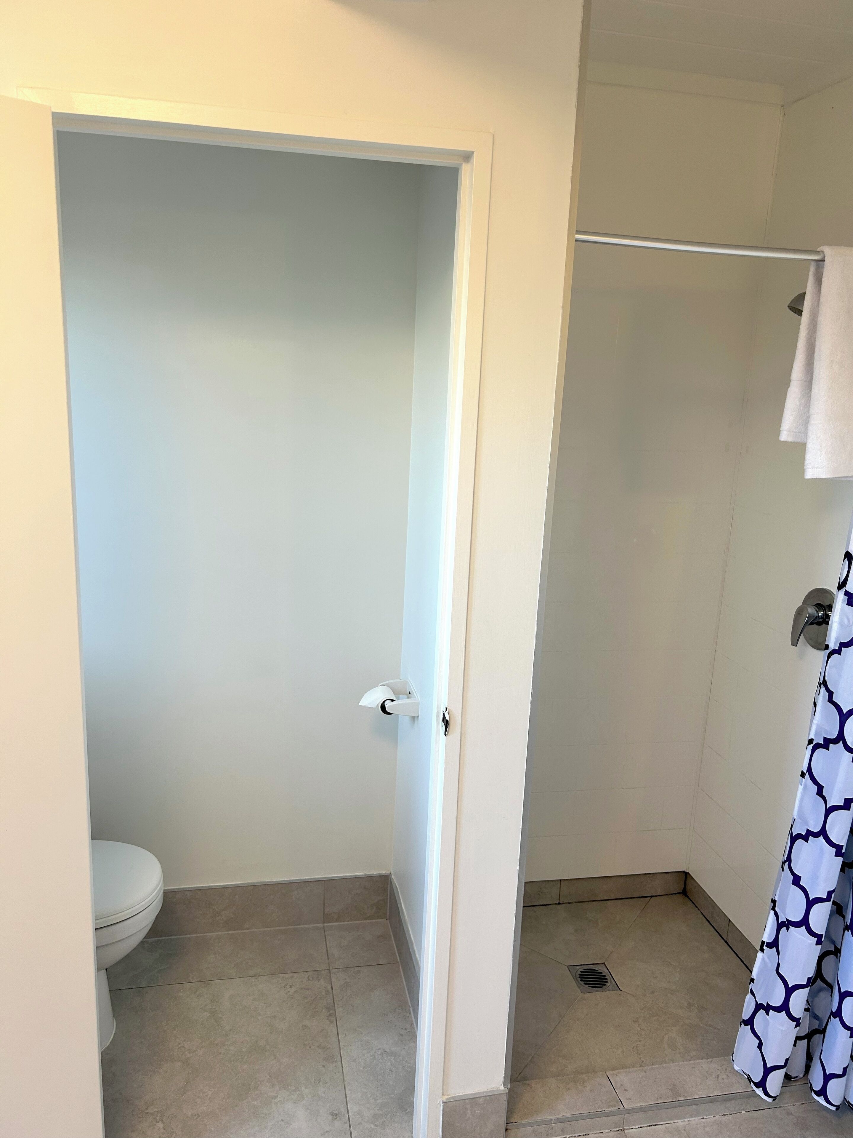Un baño con inodoro, zona de ducha y una puerta que da a otra habitación.