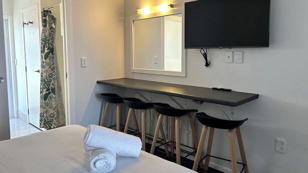 A hotel room with a bed, a desk with stools, a mirror, and a TV mounted on the wall. - Midway Motel Rotorua (Rotorua)