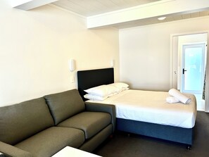 A hotel room with a bed, a grey sofa, and a door leading outside.