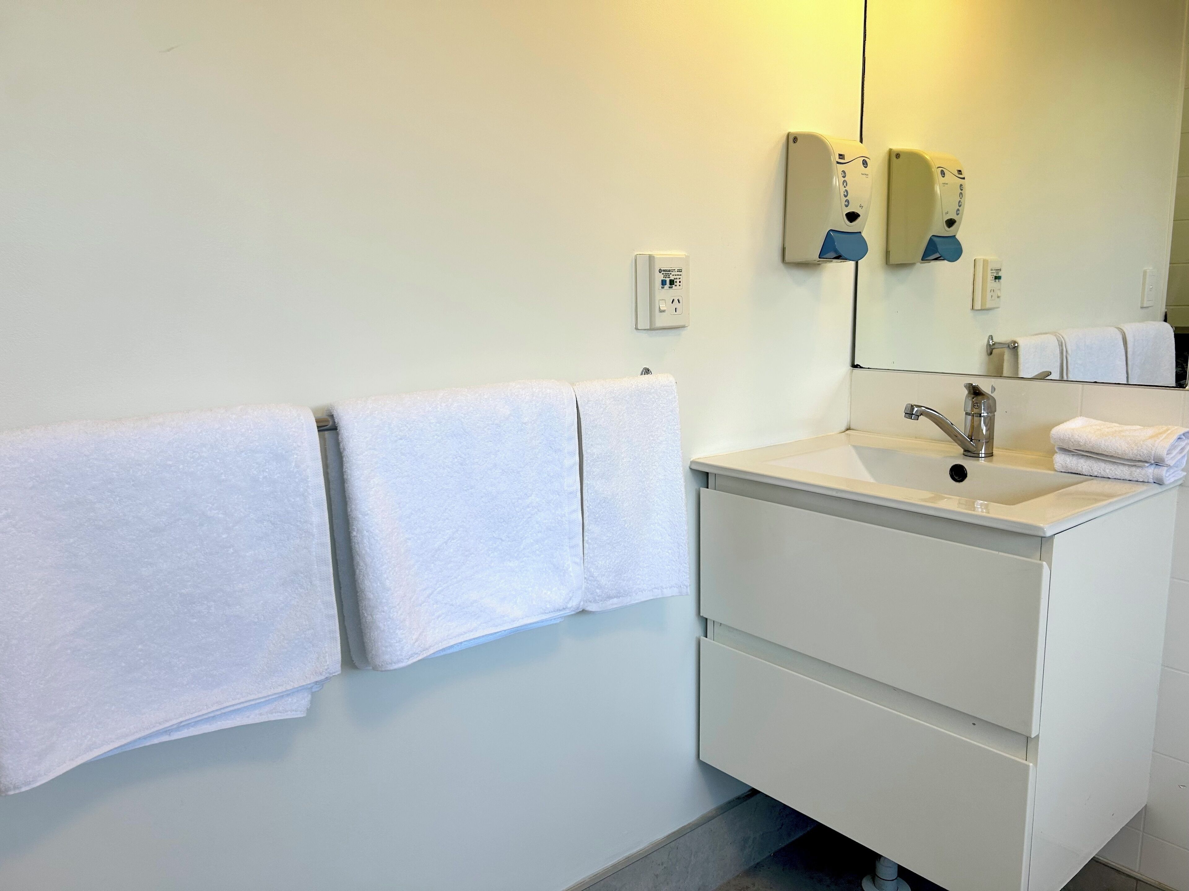 A modern bathroom with a white sink, mirror, and towel rack.