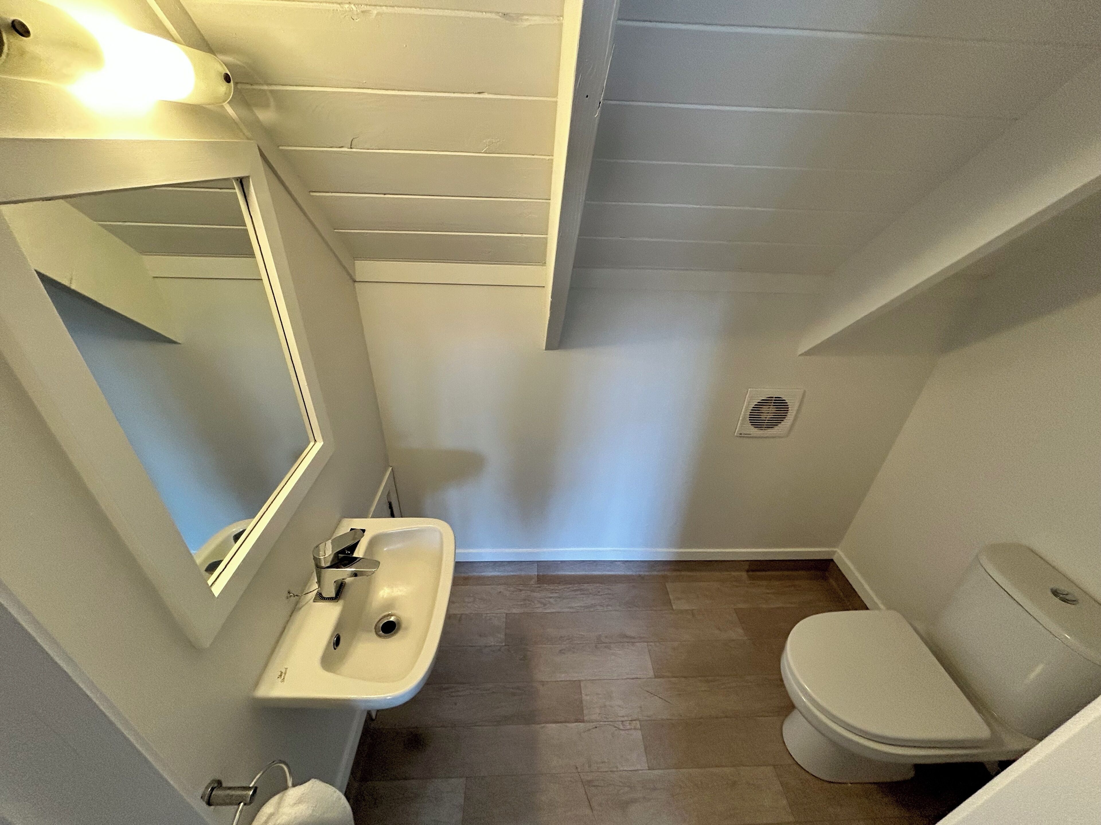 Een kleine, praktische badkamer met een wit wastafel, spiegel en toilet.