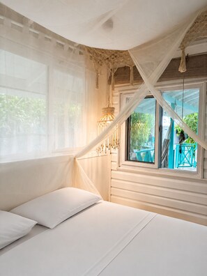 A bedroom with a canopy bed, a window with a view of outdoor furniture, and a hanging light fixture. - Siloe Cove (San Andrés)