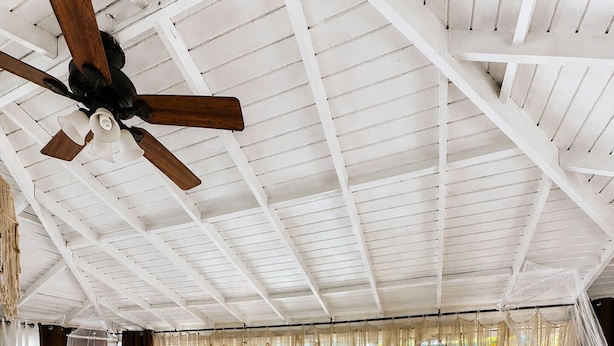 Une pièce spacieuse avec un plafond haut, un ventilateur de plafond, un lit à baldaquin, un canapé agrémenté de coussins à motifs et une table basse ornée d’objets décoratifs.