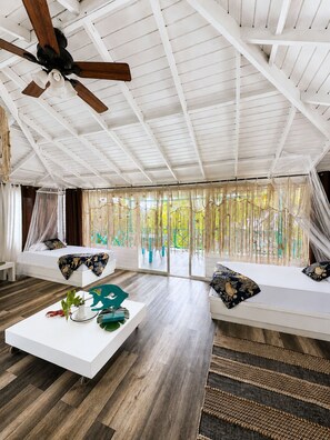 A spacious room with a high ceiling, a ceiling fan, a bed with a canopy, a sofa with patterned cushions, and a coffee table with decorative items. - Siloe Cove (San Andrés)