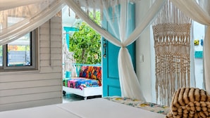 Une chambre à coucher avec un lit à baldaquin, une décoration murale en macramé et une vue sur un espace extérieur aménagé avec des sièges.