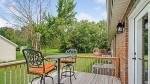 A deck with two chairs and a table, a brick wall, and a wooden railing. - Charming 2-bedroom Duplex in quaint Algood area with WiFi, HVAC, Washer-Dryer (Cookeville)