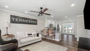 A modern living room with a white sofa, two chairs, a ceiling fan, and a kitchen area in the background. - Charming 2-bedroom Duplex in quaint Algood area with WiFi, HVAC, Washer-Dryer (Cookeville)