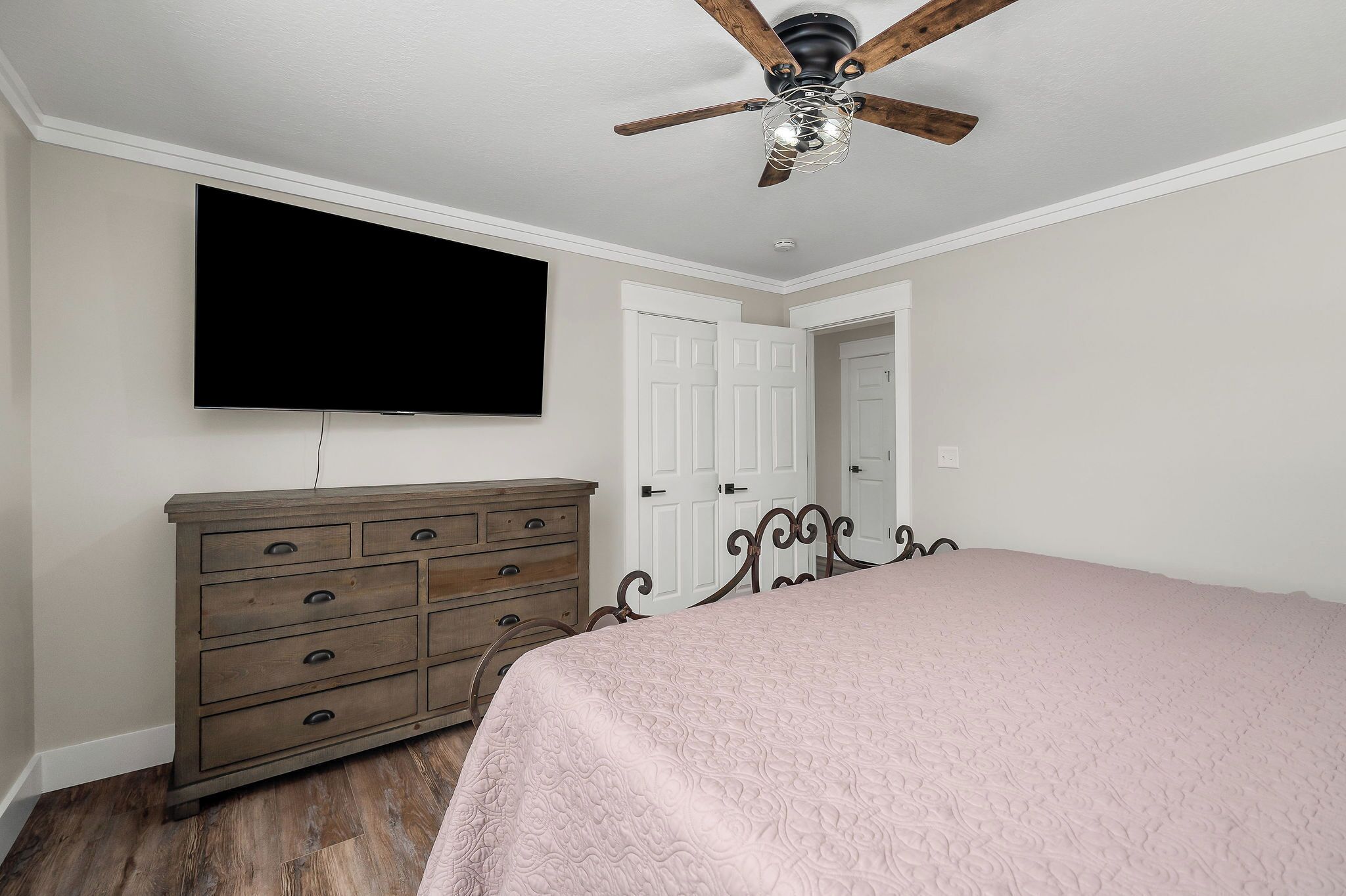 Un dormitorio con cama, cómoda, televisor, ventilador de techo y puertas blancas.