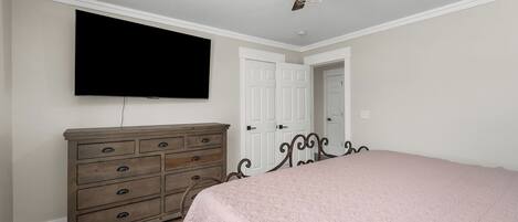 Un dormitorio con cama, cómoda, televisor, ventilador de techo y puertas blancas.