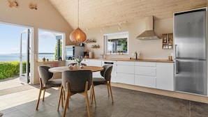 A modern kitchen with a view of the sea, featuring a dining area with a round table and chairs, a stainless steel refrigerator, and a wooden ceiling. - 1 bedroom gorgeous home in Sønder Stenderup (Sønder Stenderup)