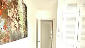 A hallway with a white tiled floor, a door at the end, and a bed with a blanket on the right.