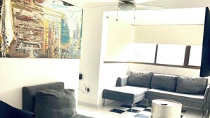 A modern living room with a checkered floor, grey sofas, a black armchair, and a ceiling fan.