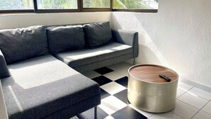A modern living room with a grey sectional sofa, a round wooden coffee table, and a black and white checkered floor.