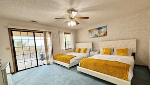 A bedroom with two beds, a ceiling fan, a window, and a view of the outdoors. - Spacious Getaway: Patio, Pool, Hot Tub, Game Room (Apple Valley)