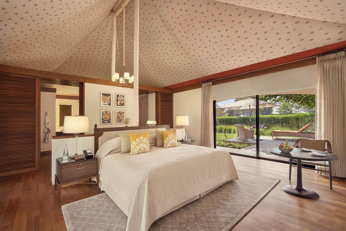 Quarto espaçoso com cama grande, mesa de cabeceira e vista do jardim através de uma porta de correr de vidro.