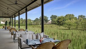 An outdoor dining area with tables and chairs, large windows, and a view of a grassy field.