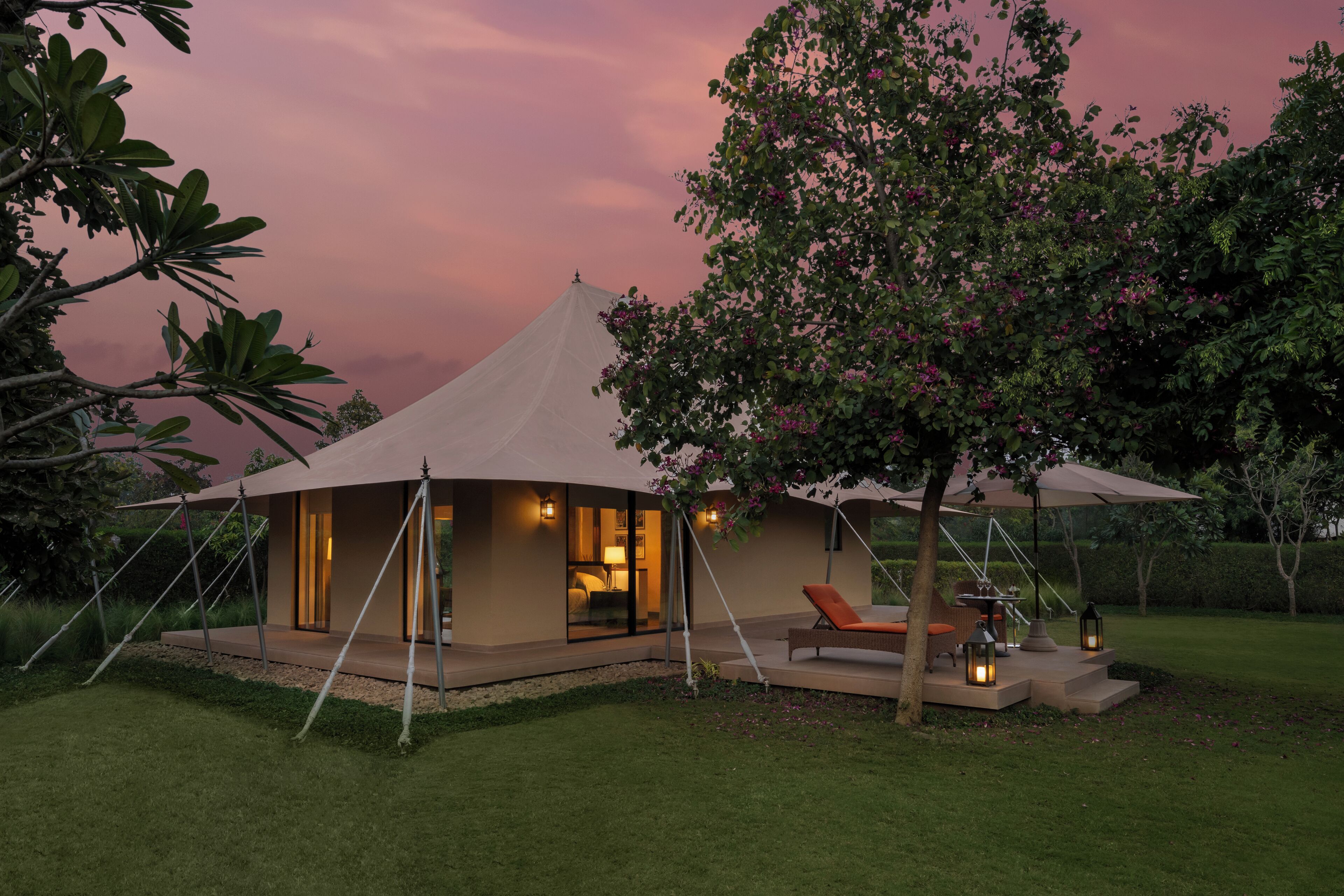 A tented accommodation with a glass facade, outdoor seating, and ambient lighting.