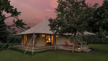 A tented accommodation with a glass facade, outdoor seating, and ambient lighting.