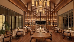 Une salle à manger spacieuse avec de hauts plafonds, des boiseries et de nombreuses tables dressées pour le repas.