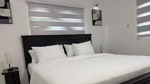 A bedroom with a large bed, white bedding, a dark headboard, and a nightstand with a lamp.