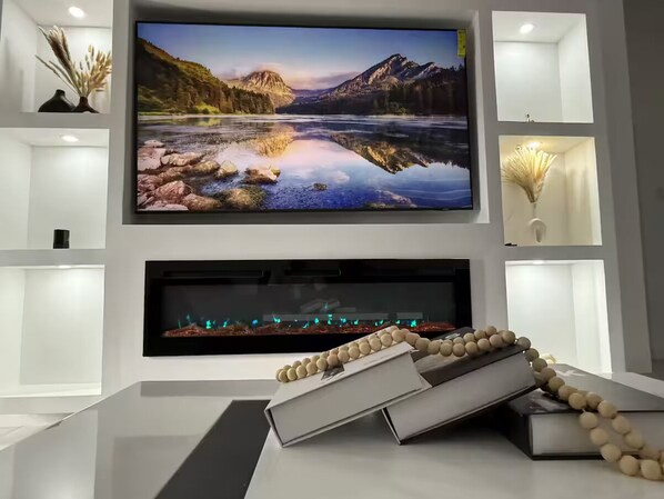 A modern living room with a large flat-screen TV mounted above a fireplace, surrounded by minimalist decor and a white console table.