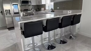 A modern kitchen with white cabinets, stainless steel appliances, a large island with bar stools, and a tiled floor.