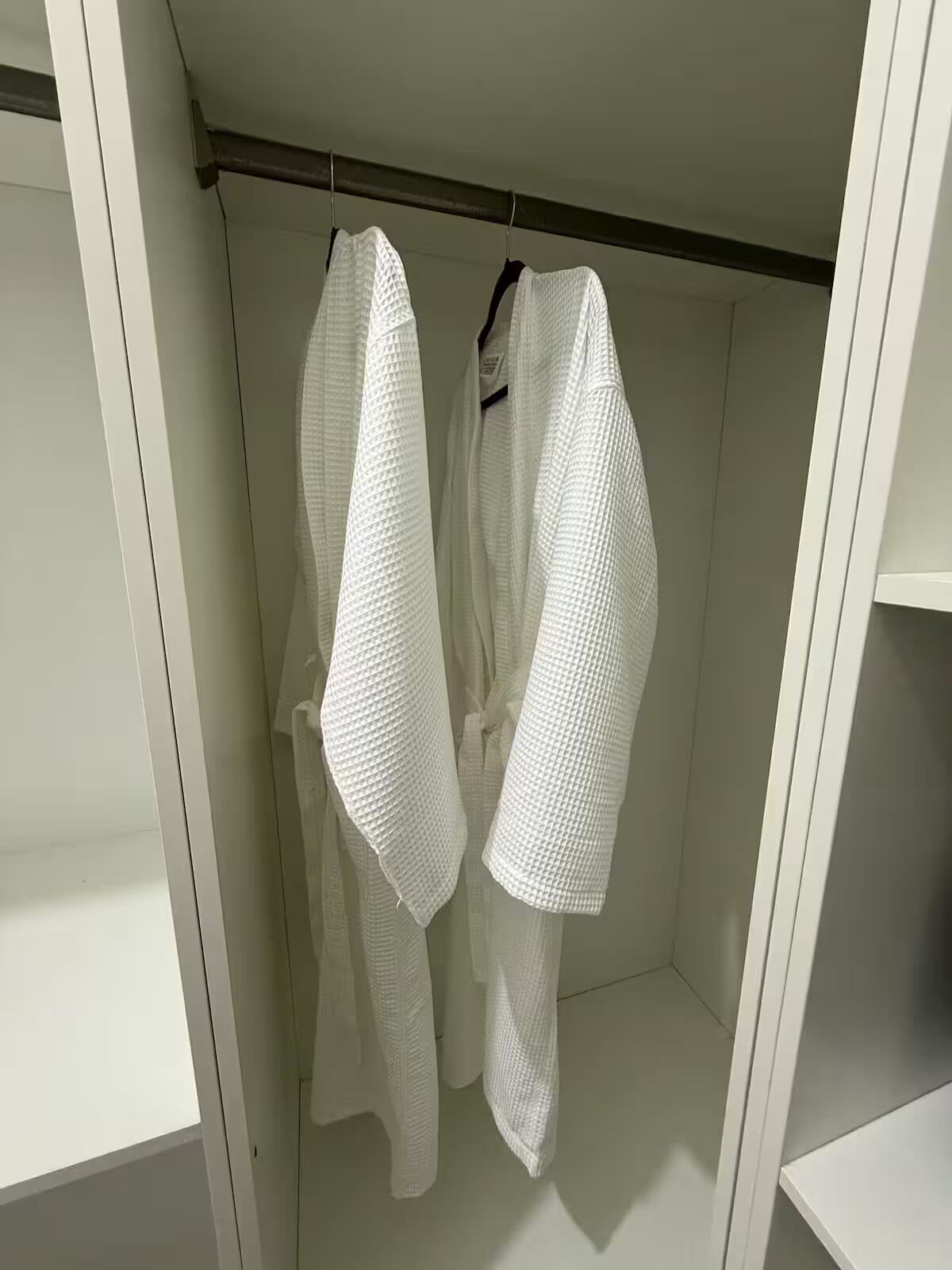 A white walk-in closet with two white robes hanging on a rod.