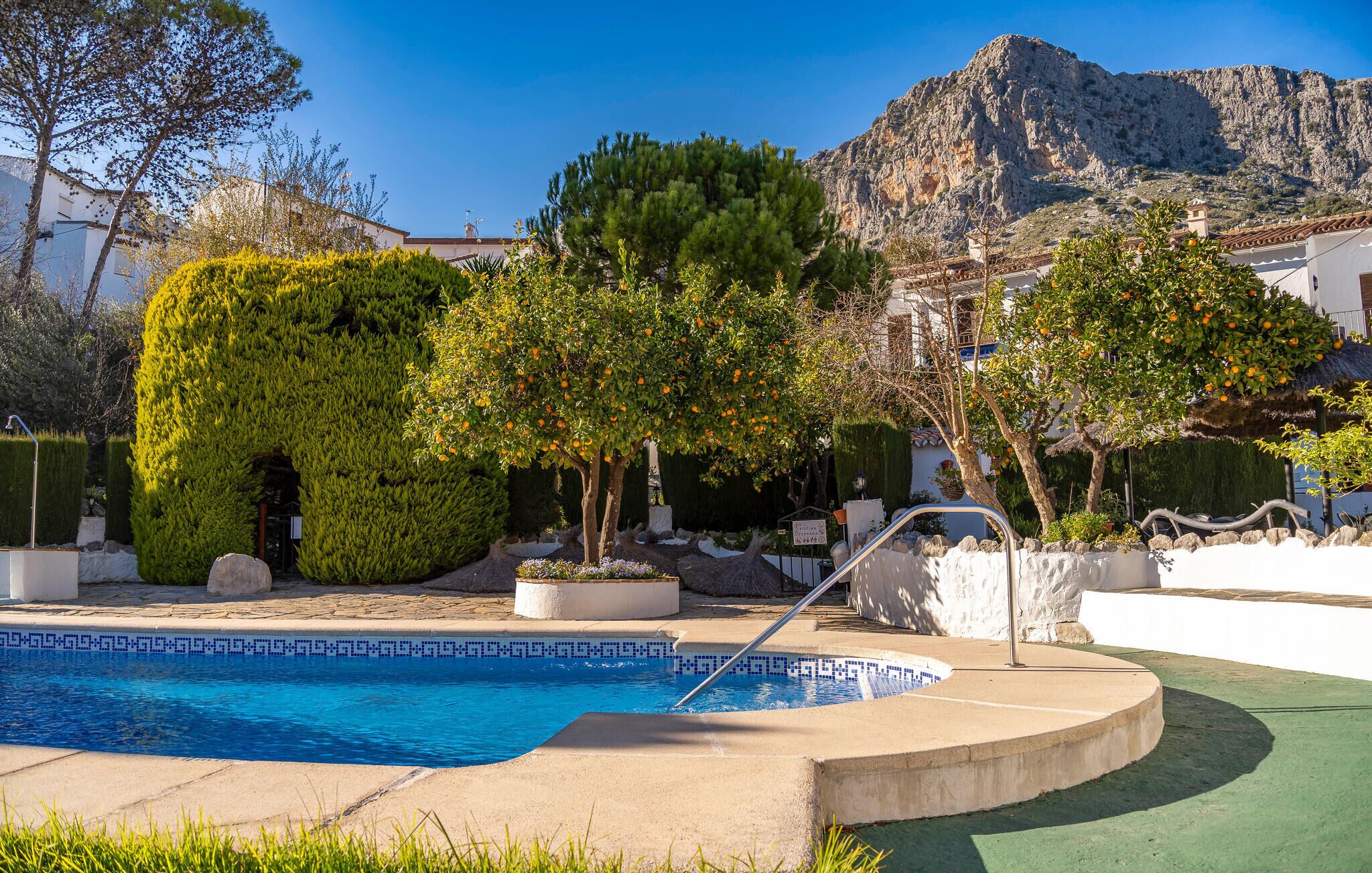 A swimming pool with a mountain backdrop, surrounded by well-maintained greenery and a white building.