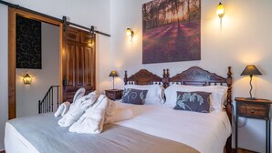 A hotel room with a large bed, a wooden door, a painting of a forest, and two wall-mounted lamps. - 2 bedroom stunning home in Montejaque (Montejaque)