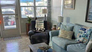 Ein Wohnzimmer mit Sofa, Sessel, Couchtisch und Blick ins Freie durch große Fenster.