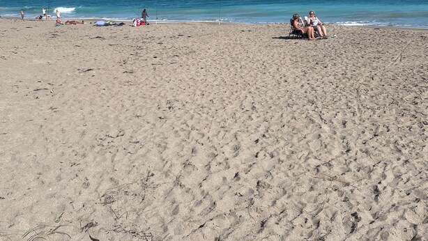 Ein Sandstrand mit blauem Himmel und ruhiger See.