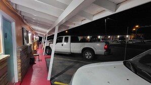 A parking area with a white truck and a white car, a red pathway, and a building with a wooden exterior and a window with a light. - Gulfway Motel By OYO Near Airport I 37 (Corpus Christi)