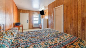 A room with wooden paneling, a bed with a patterned bedspread, a television mounted on the wall, and a door leading outside. - Gulfway Motel By OYO Near Airport I 37 (Corpus Christi)