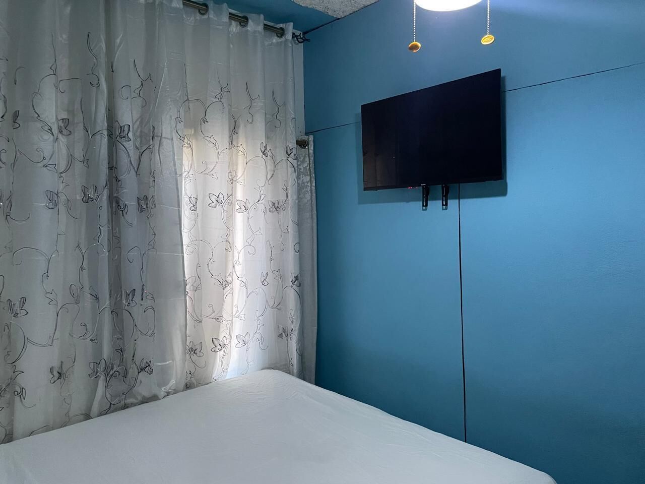 Ein Schlafzimmer mit einem Bett, einem an der Wand montierten Fernseher und einem Vorhang mit Blumenmuster.