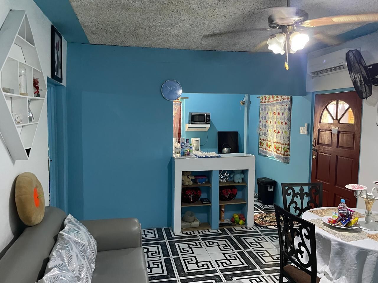 A room with blue walls, a patterned floor, a sofa, a small table with items, and a door.