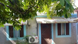 Uma casa com telhado de metal corrugado, porta azul e um pequeno alpendre com plantas em vasos.