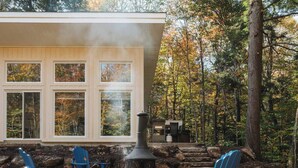 A cabin with a wood-burning stove, blue Adirondack chairs, and a stone fireplace. - Nature & Confort: 3-bedroom cottage near Tremblant (Mont-Tremblant)