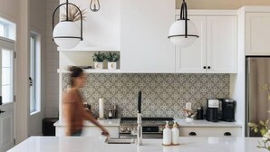 A modern kitchen with a central island, pendant lighting, and a dining area with a white chair and stools. - Nature & Confort: 3-bedroom cottage near Tremblant (Mont-Tremblant)