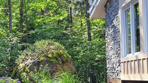 A garden with various plants and flowers, a stone building, and tall trees in the background. - Nature & Confort: 3-bedroom cottage near Tremblant (Mont-Tremblant)